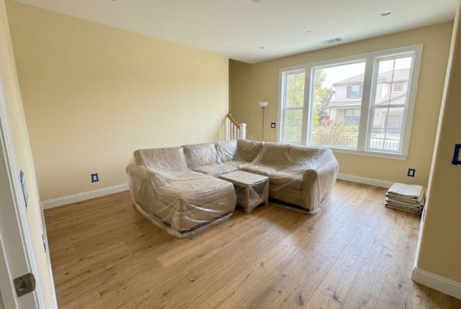 Sectional sofa and coffee table grouped in the middle of a living room and wrapped in plastic, with outlet covers removed and taped
