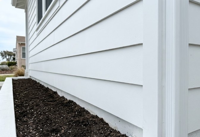White lap siding with the bottom edges of each board left open above a planter box