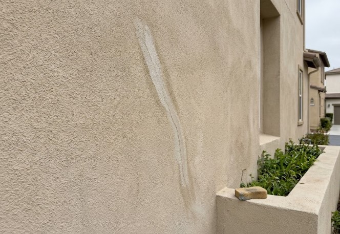 Long vertical crack in tan stucco filled with a lighter, smooth compound, with a sponge resting on the planter wall nearby